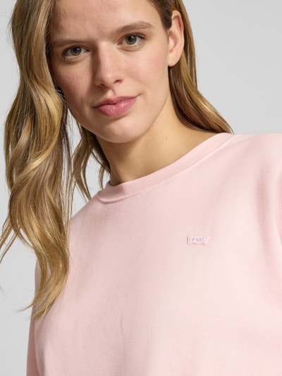 Frauenmodel trägt Sweatshirt mit gerippten Abschlüssen von Levi's®, rosa Farbton, Label-Stitching, Nahaufnahme Oberkörper.