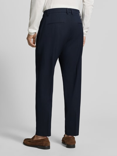 Mężczyznamodel nosi granatowe spodnie materiałowe Tapered Fit Hose mit Viskose-Anteil Modell 'Servo' von CINQUE, elastyczna mieszanka materiałów z dodatkiem wiskozy, zakładki w pasie, zapięcie na haftkę i zamek błyskawiczny, szerokość w rozmiarze 50: 51 cm, długość wewnętrzna nogawki w rozmiarze 50: 73 cm, całkowity widok z tyłu.