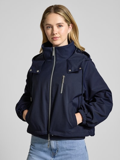 Vrouwenmodel draagt Oversized Jacke met Kapuze und Zweiwege-Reißverschluss van monari in donkerblauw met steekzakken, borstzak, taille tot op de heup, voorkant, close-up bovenlichaam.