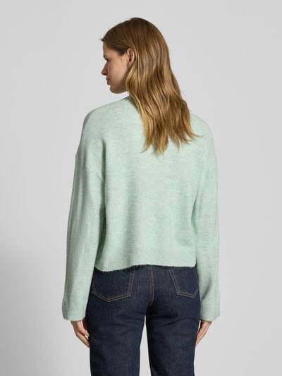 Frauenmodel trägt Relaxed Fit Strickpullover mit Crew Neck Modell 'SIMONI' von Only in mintgrüner Melange-Optik, grob gestrickt, Rumpf und Ärmel gerippt, Ganzkörperansicht Rückansicht.