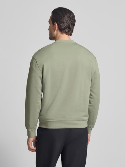 Männermodel trägt Sweatshirt mit Rundhalsausschnitt und Logo von CK Calvin Klein in Grün, Baumwoll-Elasthan-Mix, Regular-Fit, Ganzkörperansicht Rückansicht.