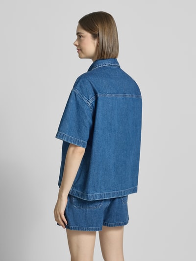 Vrouwenmodel draagt Relaxed Fit Hemdbluse in Denim-Optik model 'Lovilia' van Carhartt Work In Progress, puur katoen, borstzak, logopatch, overhemdkraag, knoopsluiting, korte mouwen, denimlook, ruglengte maat S 64 cm, mouwlengte maat S 24 cm, kleuren in denimblauw, recht silhouet, textuur glad, geheel vanaf achteren.