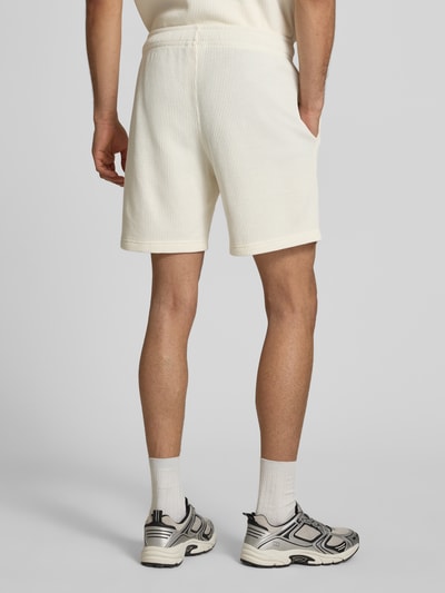 Männermodel trägt Shorts mit Strukturmuster und elastischem Bund von CHAMPION in Creme mit feiner Rippstruktur, Ganzkörperansicht Rückansicht.