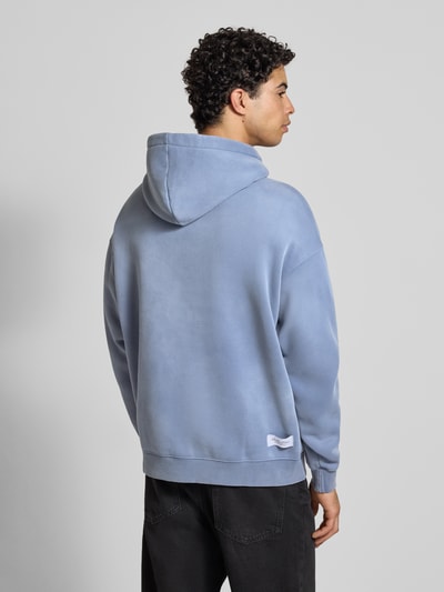 Männermodel trägt Oversized Hoodie mit Kapuze von ANOTHER COTTON LAB aus Baumwoll-Mix in Hellblau mit Label-Print, Gerippte-Abschlüsse, Känguru-Tasche, Rückenlänge 69 cm, Ärmellänge 58 cm, Ganzkörperansicht Rückansicht.