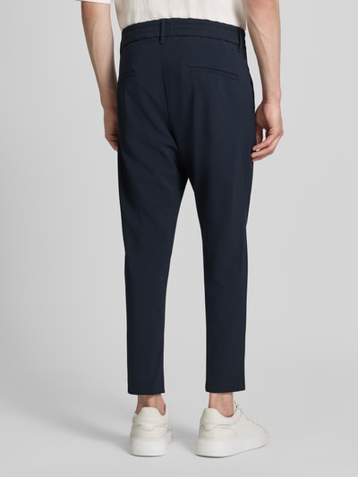 Männermodel trägt dunkelblaue Herren Hose mit Gesäßtaschen Modell 'CHASY' von Drykorn, Material-Mix, Slim-Fit, Ganzkörperansicht Rückansicht.