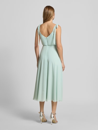 Frauenmodel trägt Knielanges Cocktailkleid mit Zierschleifen von Jake*s Cocktail in hellem Mint, taillierte Passform, Ärmelloses-Design, blickdichter Unterrock, glatter Stoff, Ganzkörperansicht Rückansicht.