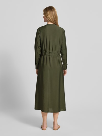 Frauenmodel trägt Relaxed Fit Midikleid aus Viskose-Mix Modell 'Mariela' von Guido Maria Kretschmer WOMAN in Oliv mit Tunnelzug und aufgesetzten Taschen, langärmeliges Design, Rückenlänge 128 cm, Rückenansicht Ganzkörperansicht.