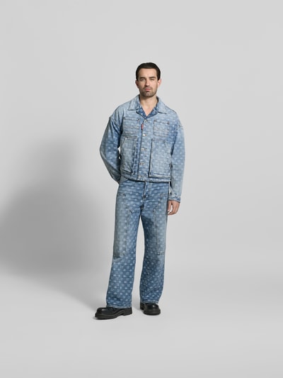 Männermodel trägt Jeansjacke aus reiner Baumwolle von Dsquared2, Regular-Fit, hellblaue Allover-Label-Stitchings, Ganzkörperansicht von vorne.