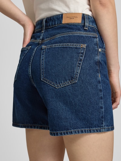Frauenmodel trägt Bermuda Leg Jeansshorts aus reiner Baumwolle von Marc O'Polo Denim in dunklem Blau mit Label Patch und 5-Pocket-Design, Ganzkörperansicht Rückansicht.