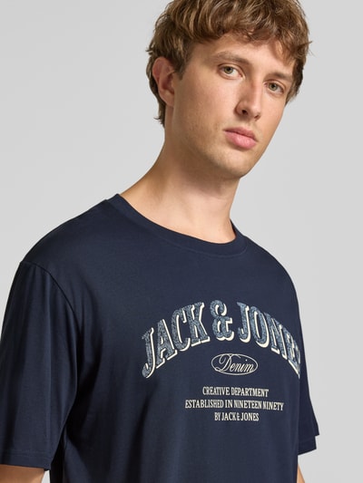 Männermodel trägt Regular Fit T-Shirt aus reiner Baumwolle Modell 'Denver' von JACK & JONES, dunkelblau mit Logo-Print, Nahaufnahme Oberkörper. Herren T-Shirt von JACK & JONES, Rückenlänge bei Größe M 69 cm, Regular Fit, reine Baumwolle.
