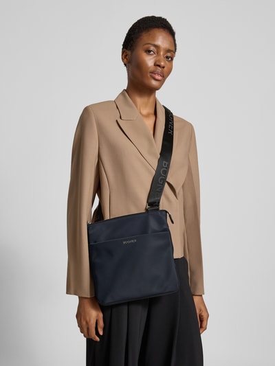 Männermodel trägt Shoulder Bag mit Logo-Detail Modell 'Serena' von BOGNER in Dunkelblau, strukturierte Oberfläche, Ganzkörperansicht von vorne, Główna przegroda z zamkiem błyskawicznym, regulowany pasek na ramię, Szerokość w rozmiarze 1: 28 cm, Długość w rozmiarze 1: 28 cm, Głębokość w rozmiarze 1: 3 cm, długość paska: 118 cm.