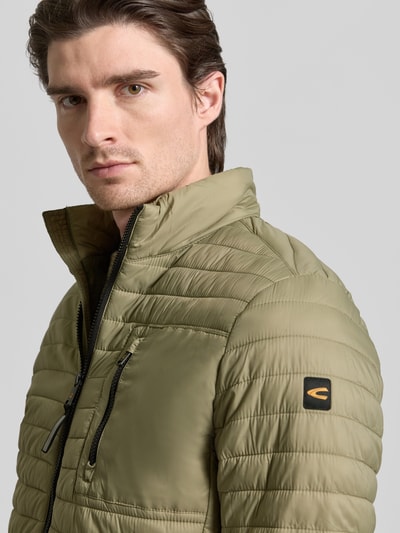 Męski model nosi Kurtka pikowana ze stójką od camel active, krój regular fit, zamek błyskawiczny, kieszenie zapinane na zamek błyskawiczny, długość tyłu w rozmiarze M: 27 cm, szerokość ramion w rozmiarze M: 19 cm, szerokość klatki piersiowej w rozmiarze M: 22 cm, długość rękawów w rozmiarze M: 27 cm, odcień oliwkowy, faktura pikowana, zbliżenie na górę ciała