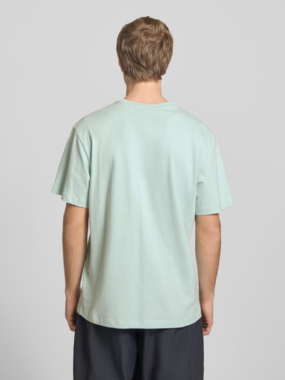 Männermodel trägt T-Shirt mit Logo-Stitching von The North Face in Mintgrün, Baumwolle, gerader Schnitt, Rückenansicht, Ganzkörperansicht Rückansicht.