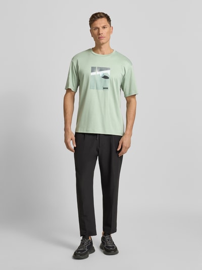 Männermodel trägt Relaxed Fit T-Shirt aus reiner Baumwolle Modell 'JOIN' von BOSS Green in Mintgrün mit Print und Label Stitching, Ganzkörperansicht von vorne.