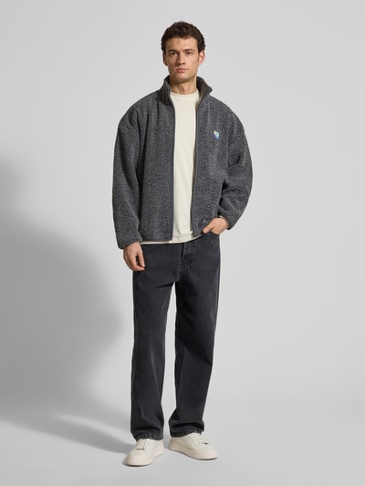 Männermodel trägt Regular Fit Jacke mit Logo-Patch von American Vintage in Grau, Kunstfell, Stehkragen, Reißverschluss, Eingrifftaschen, Ganzkörperansicht von vorne