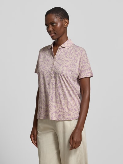 Frauenmodel trägt Relaxed Fit Poloshirt aus reiner Baumwolle von Marc O'Polo mit Optik:Allover-Muster, floralem Muster und Polokragen, in sanften Fliedertönen, Materialverarbeitung: Jersey, kurze Knopfleiste, Ärmelform: Kurzarm, Ganzkörperansicht von vorne.