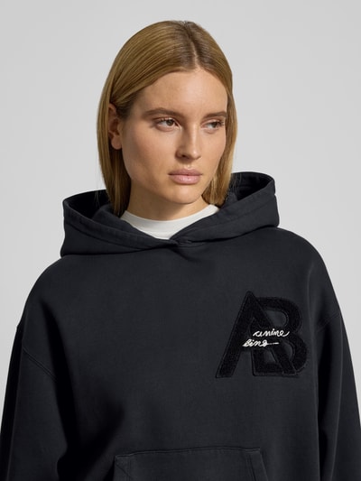 Frauenmodel trägt Regular Fit Hoodie mit Logo-Detail von Anine Bing, reine Baumwolle, Logo-Detail, Känguru-Tasche, elastische Abschlüsse, Nahaufnahme Oberkörper.