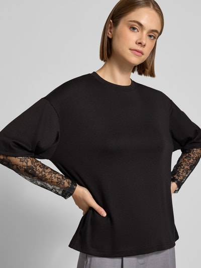 Vrouwenmodel draagt zwart shirt met lange mouwen met viscose, kanten inzetstukken aan de mouwen, Regular Fit Langarmshirt mit Viskose-Anteil model 'TAHLIA' van ONLY, Dames, detailopname bovenlichaam.