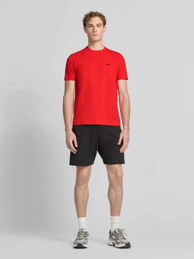 Męski model nosi Regular Fit T-Shirt aus Baumwoll-Mix von BOSS Green w intensywnie czerwonym kolorze, gładka faktura, Ganzkörperansicht von vorne.