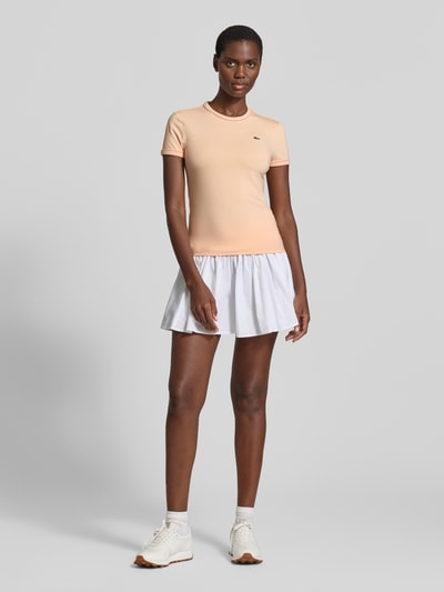 Frauenmodel trägt Slim Fit T-Shirt aus Baumwoll-Mix von Lacoste in Unifarbe mit Logo-Stitching und Kontrastpaspel, Ganzkörperansicht von vorne.