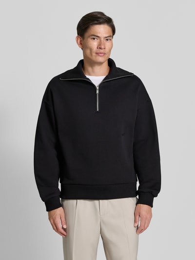 Männermodel trägt Regular Fit Sweatshirt aus Baumwoll-Mix mit Troyer-Kragen von DRYKORN, Schwarz, Logo-Stiching, Ganzkörperansicht von vorne.