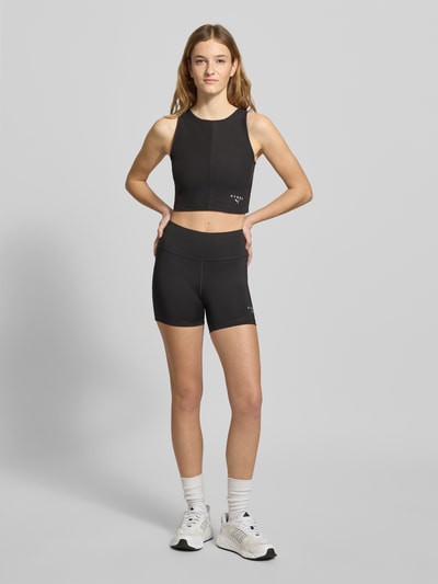 Frauenmodel trägt PUMA x HYROX - Shorts mit Label-Print von PUMA, schwarze Farbe, körpernaher Schnitt, elastischer Bund, Ganzkörperansicht von vorne.