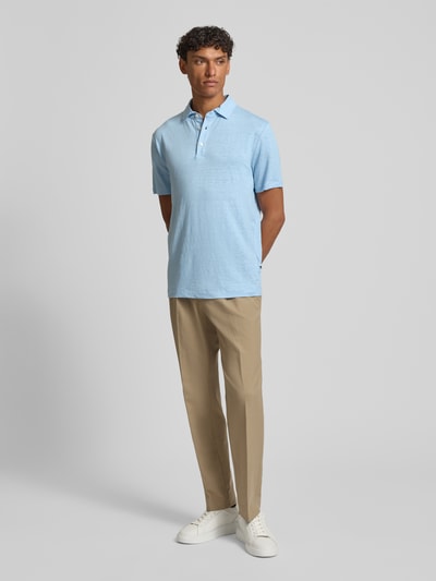 Męski model nosi Slim Fit Poloshirt aus Leinen-Elasthan-Mix von OLYMP Level Five w kolorze jasnoniebieskim, krój slim fit, półrękaw, guziki, długość tyłu w rozmiarze M: 70 cm, widok całej sylwetki od przodu.
