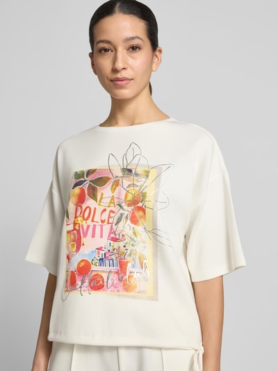 Vrouwenmodel draagt Relaxed Fit T-Shirt met Logo-Print van Christian Berg Woman, elastische materiaalmix met modal, ronde hals, kleurrijk motief met oranje- en rozennuances, close-up bovenlichaam voorkant.