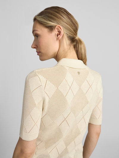 Vrouwenmodel draagt Slim Fit poloshirt met knoopsluiting model MELODY van GUESS, materiaalmix met wol, gebreid shirt, ruglengte 55 cm, mouwlengte 23 cm, beige, ruitpatroon, textuurrijke stof, detailopname rugaanzicht.