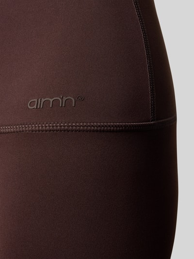 Frauenmodel trägt Leggings mit elastischem Bund Modell 'Sense' von aim'n, dunkelbrauner Stoff mit glatter Textur, Nahaufnahme Oberschenkel.