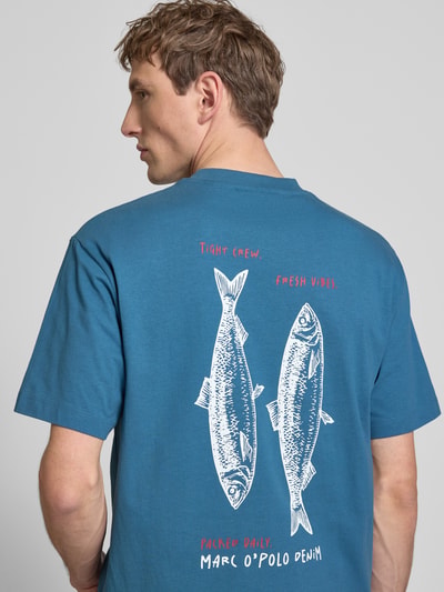 Männermodel trägt Relaxed Fit T-Shirt aus reiner Baumwolle von Marc O'Polo Denim, Optik: Regular-Fit, Motiv-Print, Label-Print, Rundhals, Kurzarm, Farbe Blau, glatte Baumwoll-Textur, Ganzkörperansicht Rückansicht.