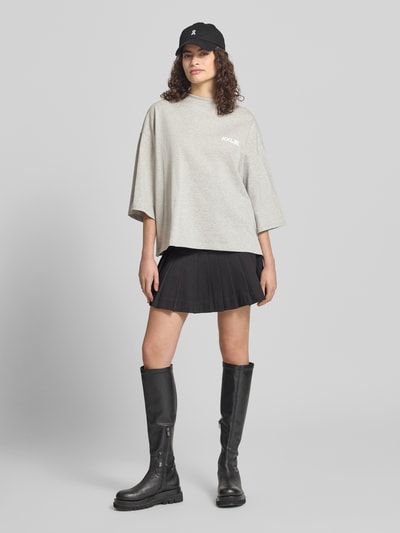 Frauenmodel trägt Oversized T-Shirt mit Rundhalsausschnitt von Karo Kauer aus bawełna, krój oversized, krój krótki, nadruk z logo, okrągły dekolt, długość tyłu w rozmiarze S: 61 cm, jasnoszary, gładka faktura, Ganzkörperansicht von vorne.