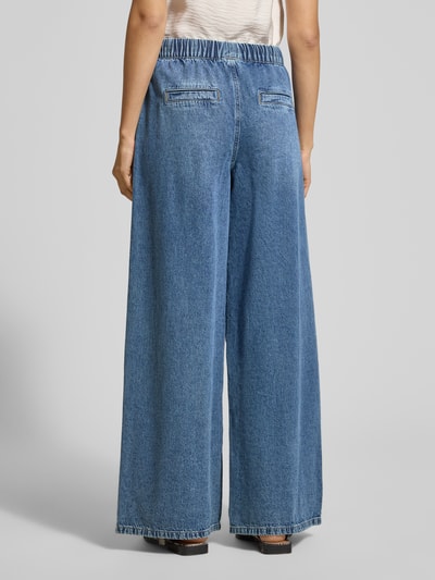 Frauenmodel trägt Wide Leg Jeans aus Baumwoll-Viskose-Mix Modell 'VALERIA' von Vero Moda in Denim-Optik, elastischer Bund, seitliche Eingrifftaschen, angedeutete Gesäßtaschen, Ganzkörperansicht Rückansicht.