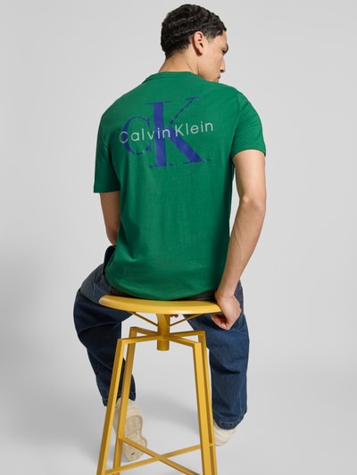 Männermodel trägt Regular Fit T-Shirt mit Logo-Print von Calvin Klein Jeans in Grün aus Baumwolle, Rückenansicht, Ganzkörperansicht Rückansicht.