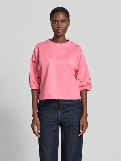 Kobiece modelka nosi t-shirt z rękawem o dł. 3/4 i haftem angielskim od Marc Cain, bawełna, krój regular fit, okrągły dekolt, długość tyłu w rozmiarze 36: 52 cm, różowy kolor, przód, całopostaciowy widok.