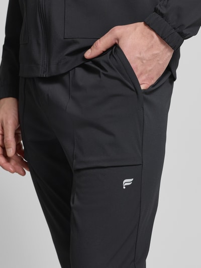 Männermodel trägt Slim Fit Sweatpants mit Logo-Print von Fabletics in Schwarz, elastischer Bund, Reißverschlusstaschen, Nahaufnahme Oberkörper.
