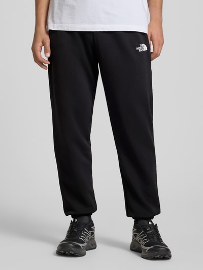 Männermodel trägt Sweatpants mit Logo-Print von The North Face in Schwarz, Baumwoll-Mix, Slim-Fit, Elastischer Bund mit Kordelzug, Ganzkörperansicht von vorne.