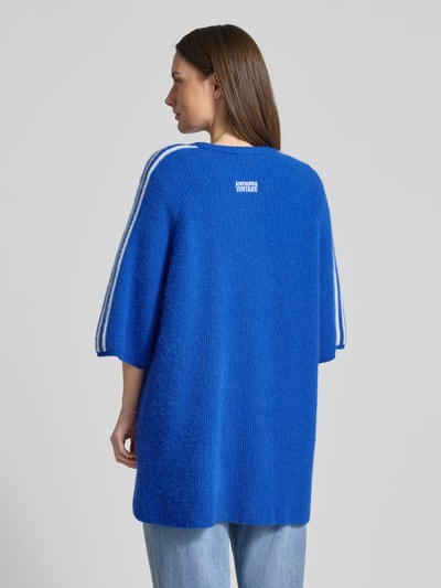 Frauenmodel trägt blaue Strickjacke in Überlänge Modell 'VITOW' von American Vintage mit weißen Streifen, gerippte Abschlüsse, lockerer Schnitt, Ganzkörperansicht Rückansicht.