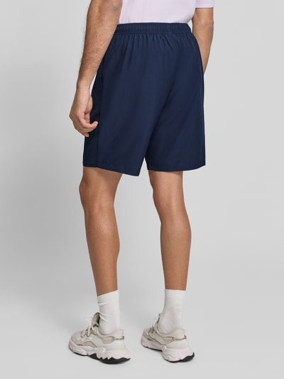Mannenmodel draagt Relaxed Fit Shorts met Logo-Patch van Lacoste Sport in donkerblauw, gladde stof, volledige lichaamsweergave achteraan.