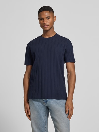 Męski model nosi Regular Fit T-Shirt aus Baumwolle od Guess, granatowy, krój regular fit, bawełna, detal z logo, jeansy, ujęcie całej sylwetki z przodu.