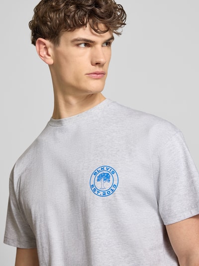 Mannelijk model draagt T-Shirt met Logo en Rondhals van BLKVIS in lichtgrijs, pure katoen, regular fit, logo op borst, borstbenadering, detailopname bovenlichaam.