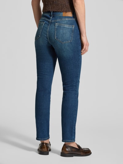 Frauenmodel trägt Slim Fit Jeans aus Baumwoll-Mix Modell 'BETSY' von s.Oliver RED LABEL in Mid Waist Denim mit Kontrastnähten, Ganzkörperansicht Rückansicht.