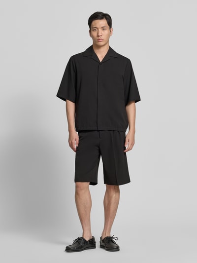 Männermodel trägt Straight Fit Shorts mit Viskose-Anteil von Lindbergh in Schwarz mit Bundfalten, Gesäßtaschen und Haken-Reißverschluss, Ganzkörperansicht von vorne.