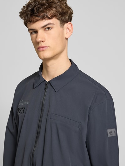 Männermodel trägt Regular Fit Hemdjacke mit Logo Modell 'HALO MOVE' von HALO, dunkel, Reißverschluss, Nahaufnahme Oberkörper. Herren Hemdjacke, Umlegekragen, Rückenlänge 66 cm, Ärmellänge 61 cm, Größe M.