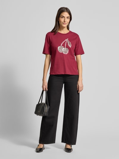 Frauenmodel trägt T-Shirt mit Motiv-Print von Marc Cain in Dunkelrot, gerade Passform, gerippter Rundhalsausschnitt, reine Baumwolle, Ganzkörperansicht von vorne.