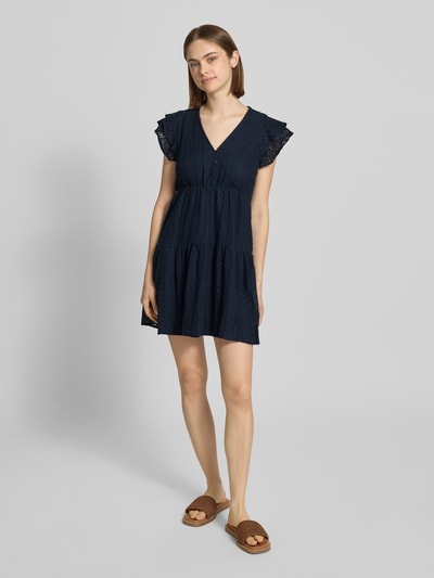 Modelka kobieca nosi tailliertes Blusenkleid aus Baumwoll-Mix Modell 'HELENA' von Only, granatowy kolor, wyhaftowane detale, krótki rękaw, długość mini, bez kołnierza, dekolt V, krótkie zapięcie na guziki, jedwabista tekstura, Szerokość w rozmiarze, Ganzkörperansicht von vorne.