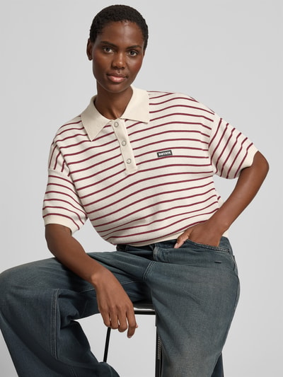 Frauenmodel trägt Relaxed Poloshirt mit Woll-Anteil von ROTATE, cremefarben mit roten Streifen, Strick-Optik, Relaxed-Fit, Nahaufnahme Oberkörper.