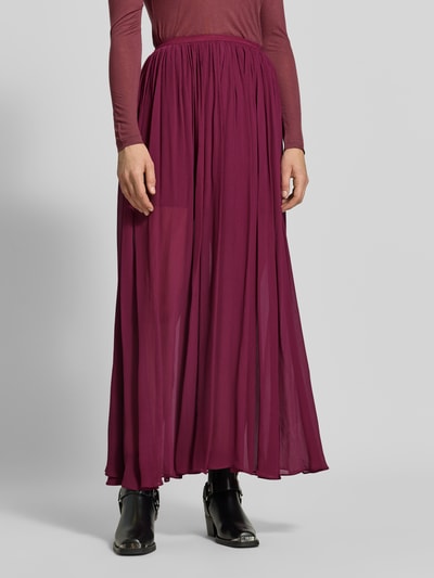Vrouwenmodel draagt Maxirock aus reiner Viskose van Anine Bing in bessenrood, rechte fit, elastische tailleband, ondoorzichte voering, plooien, detailopname onderlichaam.