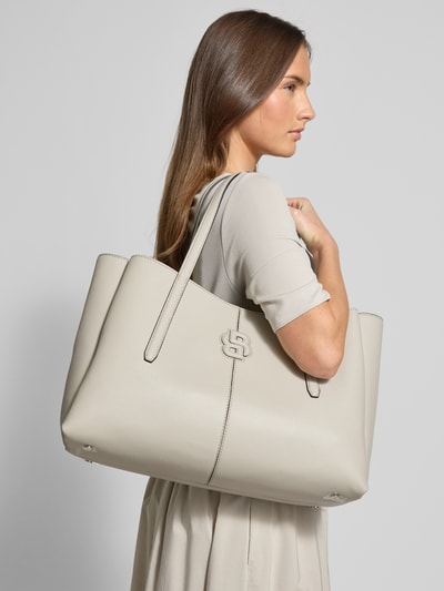 Frauenmodel trägt Shopper in Lederoptik Modell 'ANETT NEW L TOTE' von BOSS in Beige mit Logo, Karabinerverschluss, Ganzkörperansicht seitlich