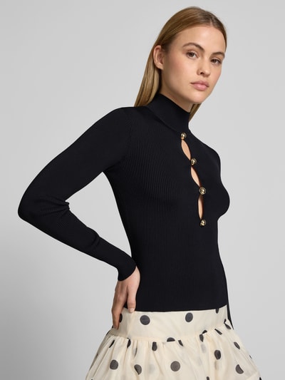 Frauenmodel trägt Slim Fit Longsleeve aus Viskose-Mix von Self-Portrait, schwarz, Cut-Outs mit Zierbesatz, Rollkragen, Nahaufnahme Oberkörper.